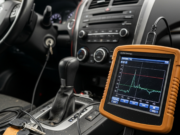 Auto ibrida: cosa cambia davvero nella manutenzione rispetto a benzina e diesel Strumento di diagnostica polveroso collegato alla presa OBD di una vettura ibrida in una comune officina indipendente.
