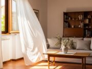 Il primo caldo di maggio ti inganna: gli errori in casa che fanno salire la bolletta Finestra socchiusa con tende mosse dalla brezza in una casa italiana, primo caldo di maggio
