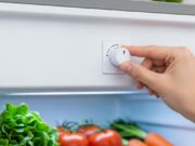 Il frigo d’estate consuma più luce e rovina il cibo: l’errore del termostato che nessuno controlla Mano che regola la manopola del termostato interno di un frigorifero aperto con verdure fresche sui ripiani