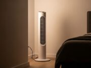Ventilatore in camera da letto: la direzione sbagliata che ti sveglia con il torcicollo Ventilatore a torre in angolo di camera da letto con luce notturna calda e letto sullo sfondo