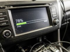 L’aggiornamento notturno che blocca l’auto prima delle vacanze: come evitarlo Schermo del cruscotto impolverato che mostra l'avanzamento di un aggiornamento software con cavi e chiavi sul tunnel centrale