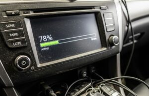 L’aggiornamento notturno che blocca l’auto prima delle vacanze: come evitarlo Schermo del cruscotto impolverato che mostra l'avanzamento di un aggiornamento software con cavi e chiavi sul tunnel centrale