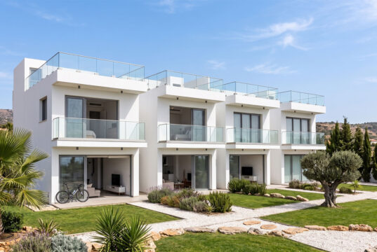 Piastrelle 30×120: il formato che valorizza gli spazi contemporanei Un complesso residenziale moderno di colore bianco con ampie balconate in vetro, giardini ben curati e un ulivo centenario, sotto un cielo azzurro e soleggiato.