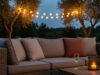 Il salotto sotto le stelle: idee per arredare la zona relax serale in giardino Divano da giardino con cuscini in lino e terracotta, calice di vino e candela su tavolino in legno, luci festoon tra gli ulivi al tramonto