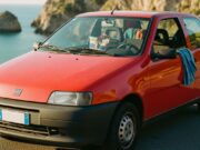 Fiat Punto: la storia dell’auto che ha portato milioni di italiani in vacanza per trent’anni Fiat Punto prima serie rossa parcheggiata su strada costiera italiana con mare sullo sfondo