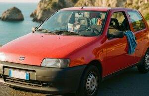 Fiat Punto: la storia dell’auto che ha portato milioni di italiani in vacanza per trent’anni Fiat Punto prima serie rossa parcheggiata su strada costiera italiana con mare sullo sfondo