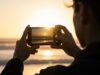 Foto in controluce con il sole: perché conviene usare il flash anche di giorno Persona fotografa il tramonto in controluce con lo smartphone in spiaggia