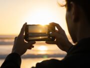 Foto in controluce con il sole: perché conviene usare il flash anche di giorno Persona fotografa il tramonto in controluce con lo smartphone in spiaggia
