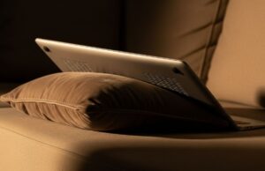 Il laptop sul divano d’estate: la presa d’aria bloccata che accumula danni invisibili sulla scheda madre Laptop appoggiato su cuscino di divano con griglie di ventilazione ostruite dal tessuto morbido