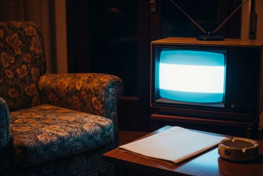 Drive In, il programma degli anni ’80 che cambiò la domenica sera italiana per sempre Televisore CRT anni '80 acceso in un salotto italiano buio con poltrona a fiori e posacenere sul tavolino