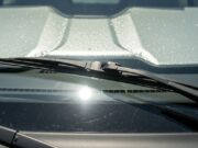 Tergicristalli alzati sotto il sole d’estate: il gesto che sembra giusto e rovina le spazzole Tergicristalli alzati sul parabrezza di un'auto parcheggiata al sole estivo con parasole riflettente interno visibile