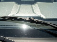 Tergicristalli alzati sotto il sole d’estate: il gesto che sembra giusto e rovina le spazzole Tergicristalli alzati sul parabrezza di un'auto parcheggiata al sole estivo con parasole riflettente interno visibile