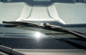 Tergicristalli alzati sotto il sole d’estate: il gesto che sembra giusto e rovina le spazzole Tergicristalli alzati sul parabrezza di un'auto parcheggiata al sole estivo con parasole riflettente interno visibile