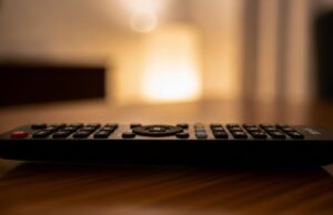 Affari Tuoi sparisce dai palinsesti serali: quando torna e cosa lo sostituisce Telecomando su tavolo in un salotto di sera, simbolo del cambio di palinsesto TV serale