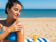 Crema solare in spiaggia: il calore la rende inutile prima di quanto pensi Donna applica la crema solare sulla spalla in spiaggia, con il tubetto appoggiato sull'asciugamano a righe