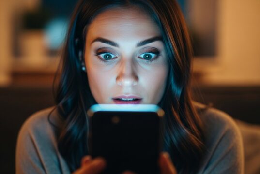 Le foto che cancelli dal telefono non sono sparite: chi può ancora vederle Donna sorpresa mentre guarda lo schermo di uno smartphone acceso al buio, illuminata dal bagliore del display
