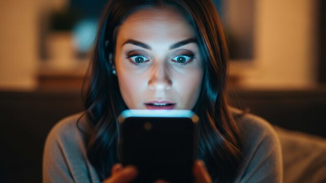 Le foto che cancelli dal telefono non sono sparite: chi può ancora vederle Donna sorpresa mentre guarda lo schermo di uno smartphone acceso al buio, illuminata dal bagliore del display