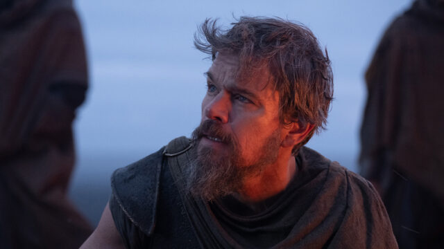 Matt Damon con barba e abiti di scena logori interpreta Ulisse, con il volto illuminato dal bagliore di un fuoco nel film Odissea di Christopher Nolan.