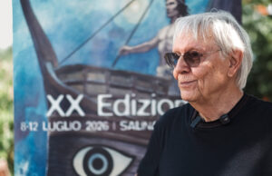 Milo Manara disegna la sua Odissea al SalinaDocFest, mentre il cinema aspetta quella di Nolan Milo Manara al SalinaDocFest 2026 davanti al poster dell'Odissea, XX edizione del festival a Salina