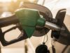 Riempire il serbatoio fino all’orlo d’estate: ecco quanti litri di benzina in eccesso rischi di perdere Pistola erogatore di benzina verde inserita nel serbatoio di un'auto durante il rifornimento estivo, con gocce di carburante sul bocchettone