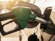 Riempire il serbatoio fino all’orlo d’estate: ecco quanti litri di benzina in eccesso rischi di perdere Pistola erogatore di benzina verde inserita nel serbatoio di un'auto durante il rifornimento estivo, con gocce di carburante sul bocchettone
