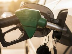 Riempire il serbatoio fino all’orlo d’estate: ecco quanti litri di benzina in eccesso rischi di perdere Pistola erogatore di benzina verde inserita nel serbatoio di un'auto durante il rifornimento estivo, con gocce di carburante sul bocchettone