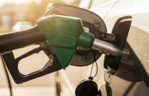 Riempire il serbatoio fino all’orlo d’estate: ecco quanti litri di benzina in eccesso rischi di perdere Pistola erogatore di benzina verde inserita nel serbatoio di un'auto durante il rifornimento estivo, con gocce di carburante sul bocchettone