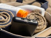 Power bank schiacciato in spiaggia: il vero motivo del rigonfiamento non è il caldo Power bank nero schiacciato in borsa da spiaggia con asciugamano, crema solare e libro, crepa visibile vicino alle porte USB