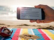 Diciamo che siamo in ferie, ma il telefono sa che non è vero Mano che regge uno smartphone con una mail di lavoro urgente in spiaggia, simbolo del quiet vacationing e della difficoltà a staccare in vacanza