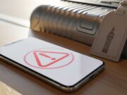 Roaming gratis nel Regno Unito: finito per quasi tutti, ecco chi lo paga da quest’estate Smartphone con icona di allarme rossa appoggiato su tavolino di legno accanto a una valigia con etichetta raffigurante Big Ben
