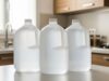 Acqua che salta in casa quest’estate: la scorta d’emergenza da preparare subito Tre bottiglioni di plastica trasparente pieni d'acqua allineati su un bancone di cucina illuminato da luce naturale