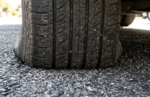 Vibrazioni al volante al rientro dalle vacanze: il vero motivo delle gomme ovalizzate Primo piano del battistrada di un pneumatico appoggiato sull'asfalto, dettaglio della zona di contatto a terra dopo una lunga sosta