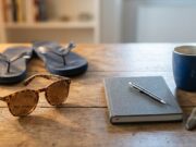 Sindrome da rientro: la statistica del 35% che gira da anni è una bufala Occhiali da sole con sabbia e infradito accanto ad agenda, penna, tazza di caffè e orologio su scrivania in legno, simbolo del passaggio dalle vacanze al rientro