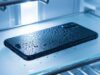 Telefono in frigorifero per raffreddarlo dopo il caldo: il danno che si vede solo dopo Smartphone nero coperto di gocce di condensa appoggiato su un ripiano di vetro dentro il frigorifero