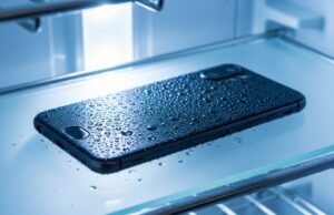 Telefono in frigorifero per raffreddarlo dopo il caldo: il danno che si vede solo dopo Smartphone nero coperto di gocce di condensa appoggiato su un ripiano di vetro dentro il frigorifero