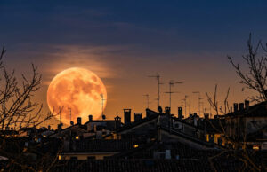 Luna del Cacciatore 2026: il 26 ottobre sembra enorme, non è come pensi Luna del Cacciatore gigante e arancione che sorge dietro i tetti di un centro storico italiano al tramonto