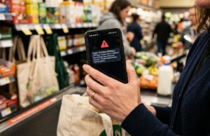 Sms falso che sembra dell’Agenzia delle Entrate: il dettaglio nel testo che lo tradisce Smartphone con falso avviso di allarme urgente in mano durante la spesa, esempio di truffa sms