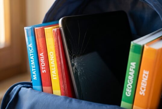 Il tablet nello zaino di scuola si rompe dall’interno: il gesto quotidiano che nessuno nota Tablet con schermo incrinato a ragnatela incastrato tra i libri scolastici colorati dentro uno zaino blu
