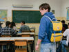 Lo zaino Invicta comprato a rate dai genitori: il vero motivo del suo successo Ragazzo con zaino Invicta giallo e blu anni '90 in un'aula scolastica