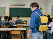 Lo zaino Invicta comprato a rate dai genitori: il vero motivo del suo successo Ragazzo con zaino Invicta giallo e blu anni '90 in un'aula scolastica
