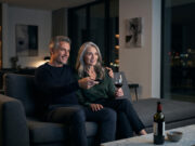 Gli italiani guardano un film ogni 4 giorni, ma sempre meno in sala: i dati Anica Coppia over 50 guarda un film in streaming la sera sul divano di casa con un bicchiere di vino