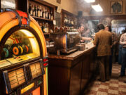 Il 45 giri dei jukebox nei bar italiani: perché non si trovava in negozio Jukebox vintage acceso in un bar italiano degli anni '70, con dischi a 45 giri visibili dietro il vetro e avventori al bancone sullo sfondo