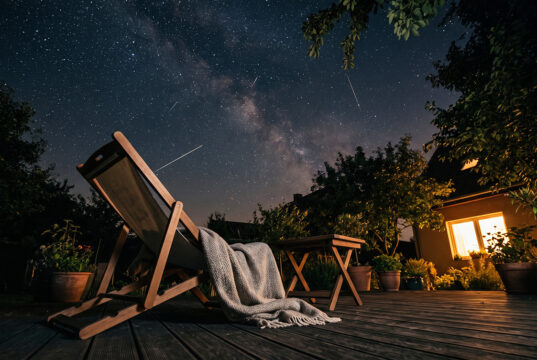 Stelle cadenti stanotte: il motivo per cui in tanti non ne vedranno nessuna Sdraio vuota con plaid su una terrazza di notte, sotto un cielo stellato con alcune scie di stelle cadenti visibili a occhio nudo