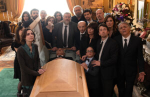 La nuova commedia di Massimiliano Bruno è al cinema da oggi, ma la storia non è affatto nuova Il cast di Un tranquillo funerale di famiglia riunito attorno alla bara durante una scena del film di Massimiliano Bruno