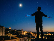 “Volare” vinse due Grammy nel 1959: il primato che nessun’altra canzone italiana ha più battuto Sagoma di una persona di spalle con le mani dipinte di blu rivolta verso un cielo notturno stellato con la luna, sopra i tetti di un borgo italiano, immagine concettuale ispirata alla canzone Volare di Domenico Modugno