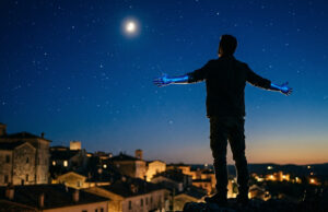 “Volare” vinse due Grammy nel 1959: il primato che nessun’altra canzone italiana ha più battuto Sagoma di una persona di spalle con le mani dipinte di blu rivolta verso un cielo notturno stellato con la luna, sopra i tetti di un borgo italiano, immagine concettuale ispirata alla canzone Volare di Domenico Modugno